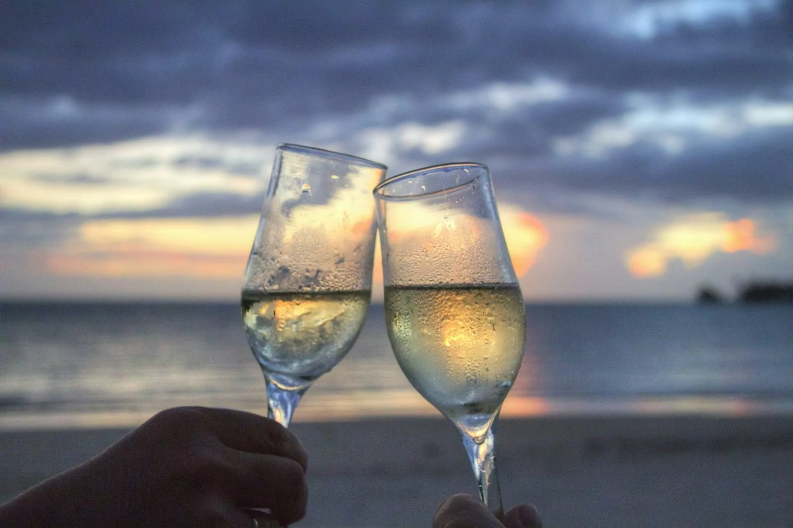 Photo by Pixabay Two champagne glasses clink at sunset on a serene beach, evoking romance and celebration.